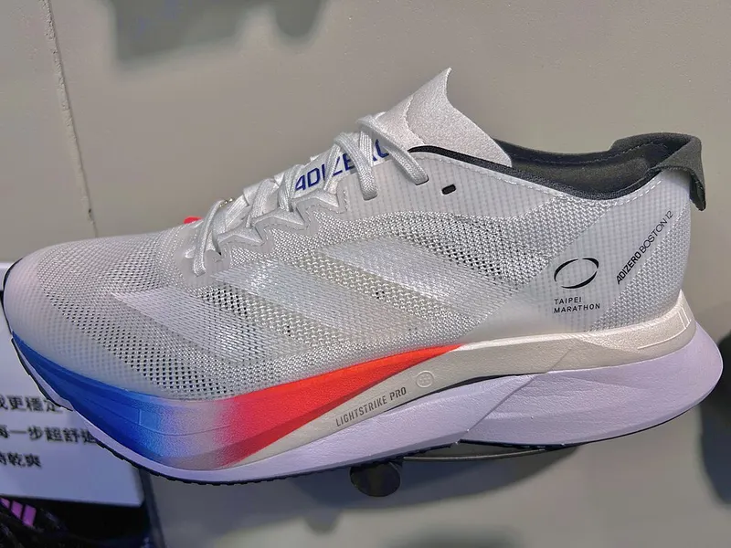 Zapatilla Adidas Adizero Boston 12 blanca con detalles rojos y azules.
